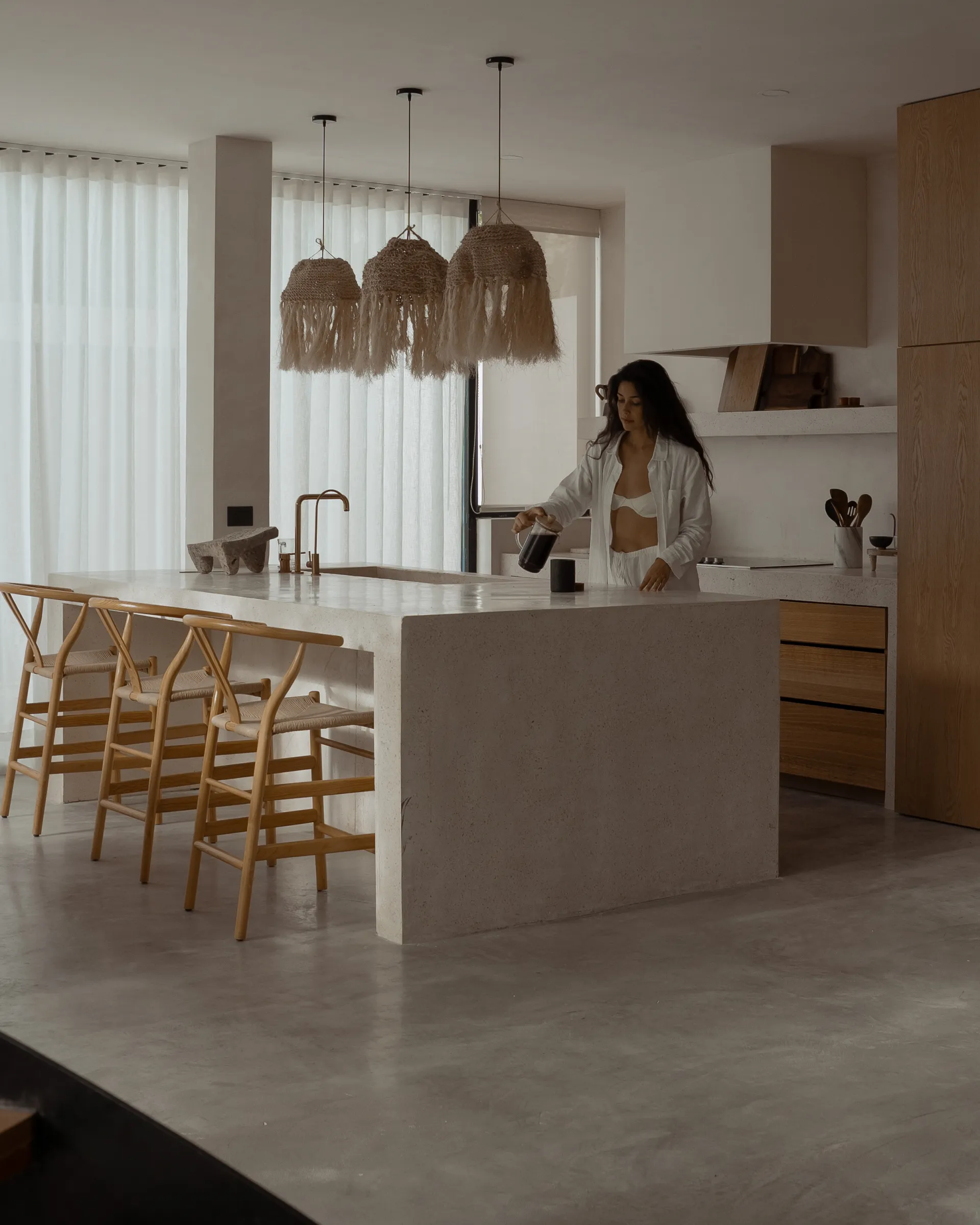 Woman making coffee in minimalist villa kitchen with pendant lights
