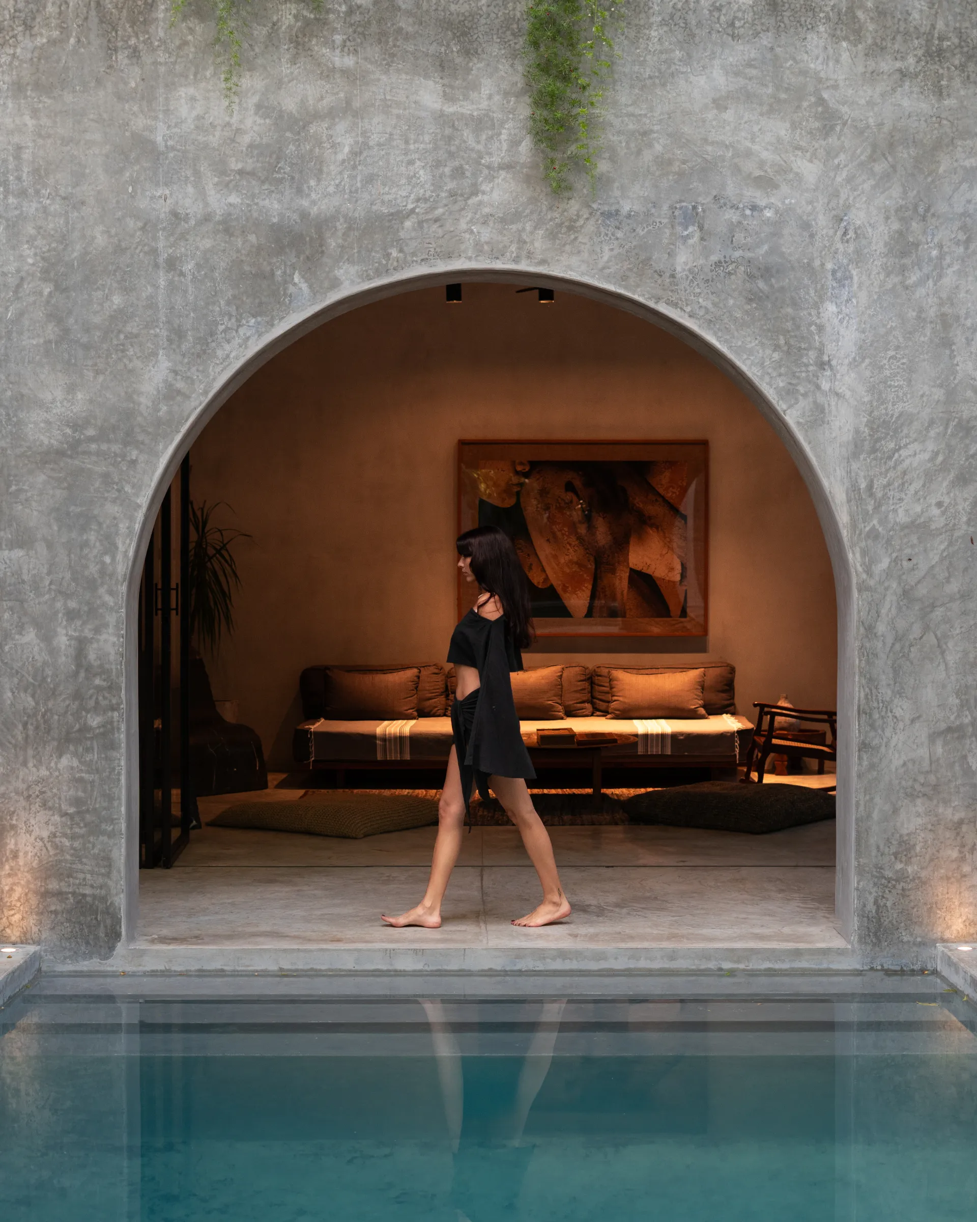 Woman walking beside pool at Casa Shalva with arched lounge behind