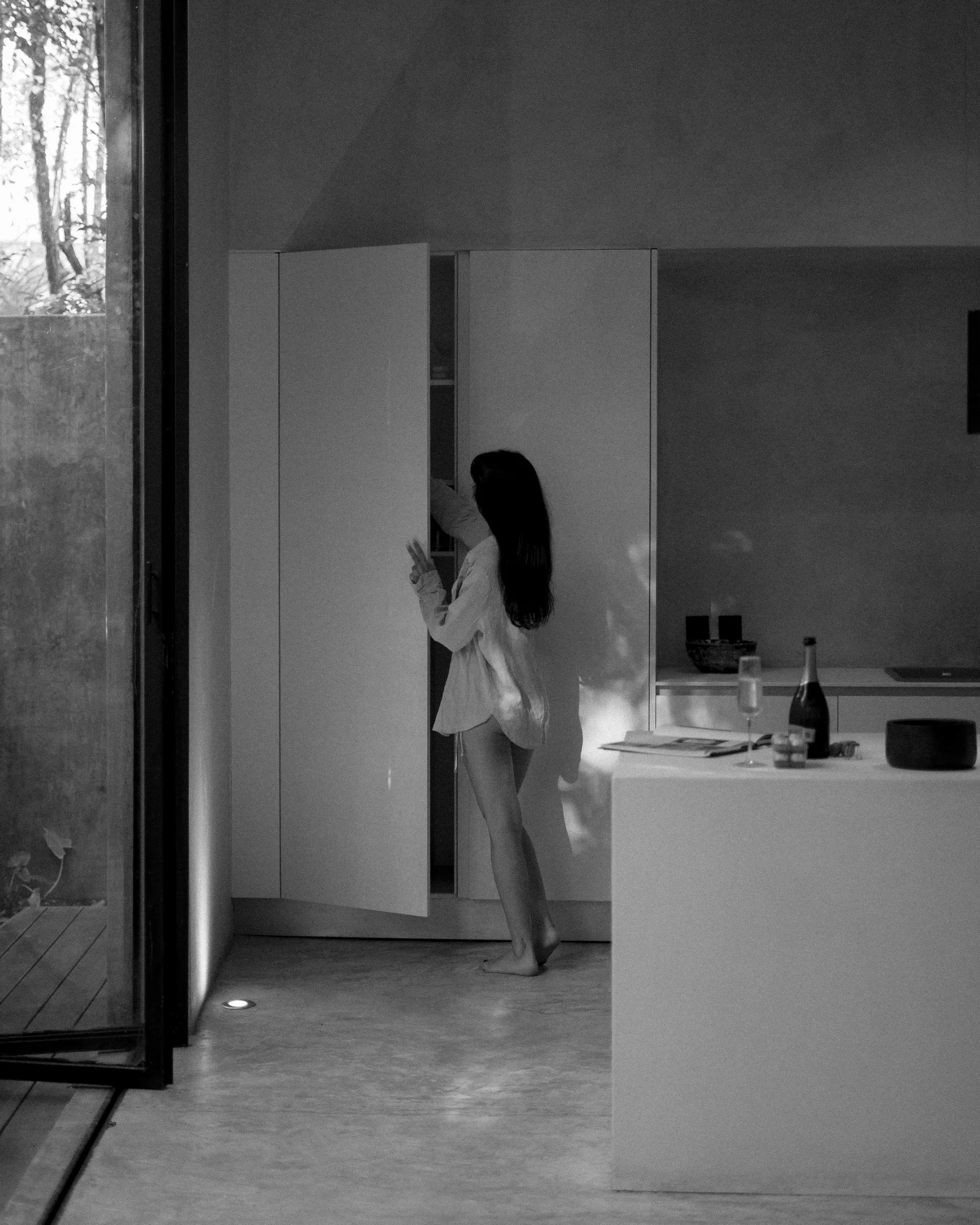 Woman in minimalist villa kitchen with jungle views through window