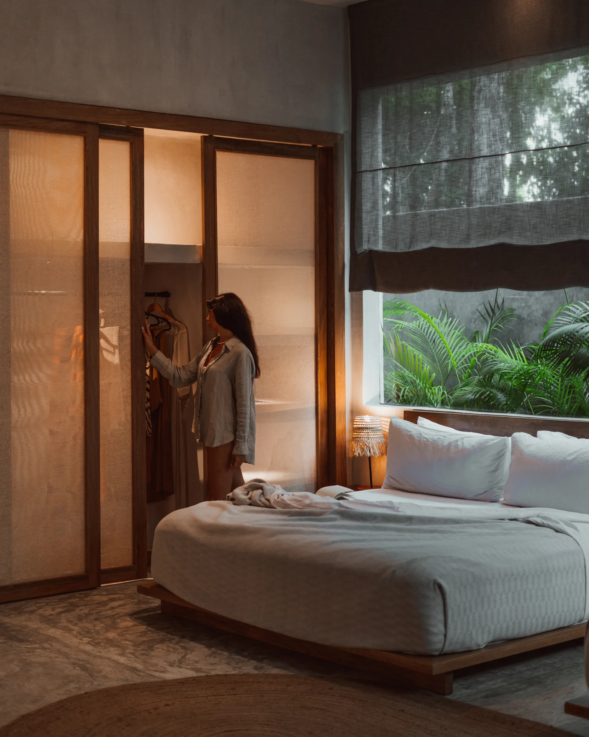 Woman selecting clothes from closet in sunlit Tulum villa bedroom