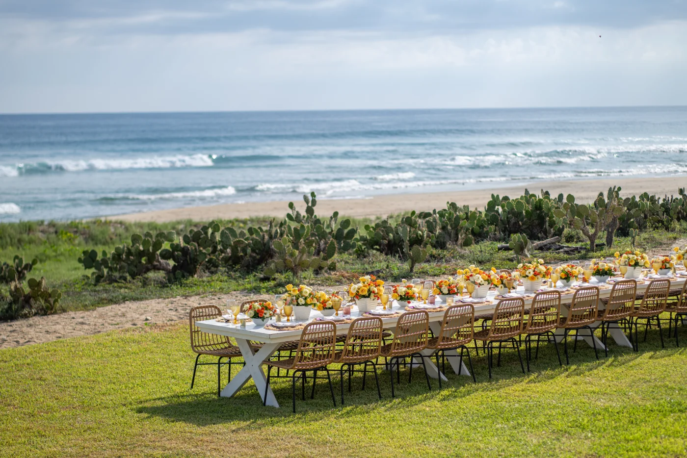 Long dinner table set for group dining on oceanfront lawn with cactus landscape