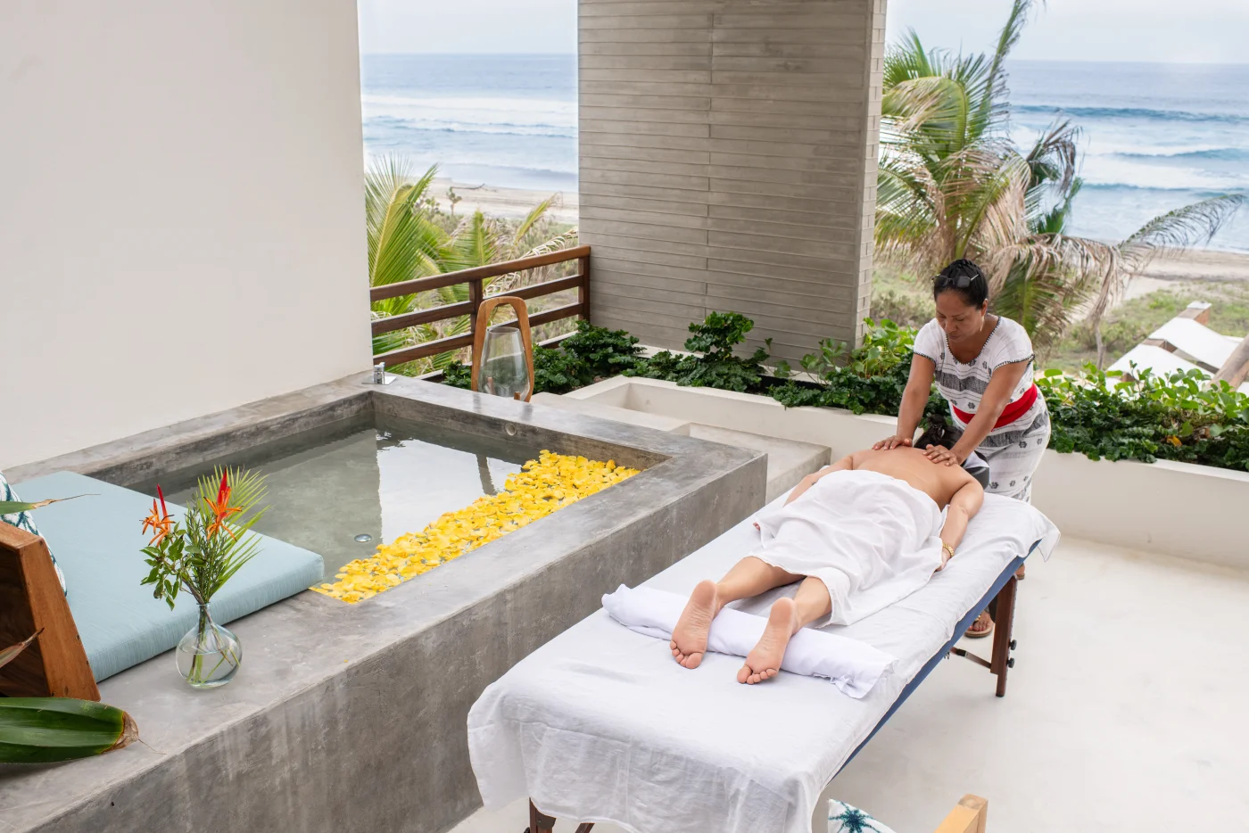 Woman receiving massage at oceanfront villa spa with flower petal bath