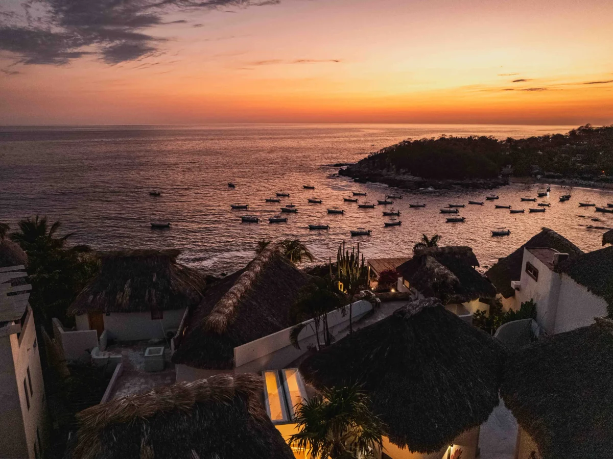 Aerial sunset over Puerto Escondido bay with fishing boats and palapa rooftops