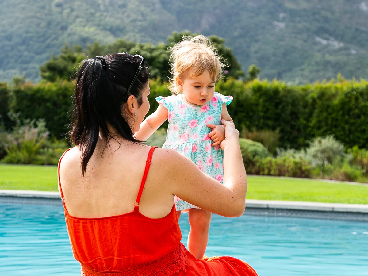 A woman in a red dress holding a child beside a villa pool in Cape Town
