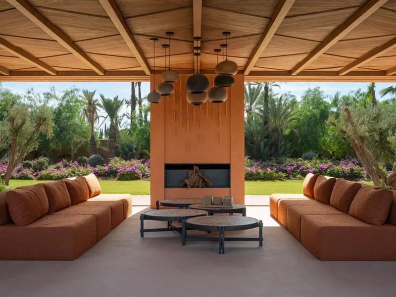 Outdoor salon under a villa pavilion, terracotta sofas and clay pendant lights against a palm garden