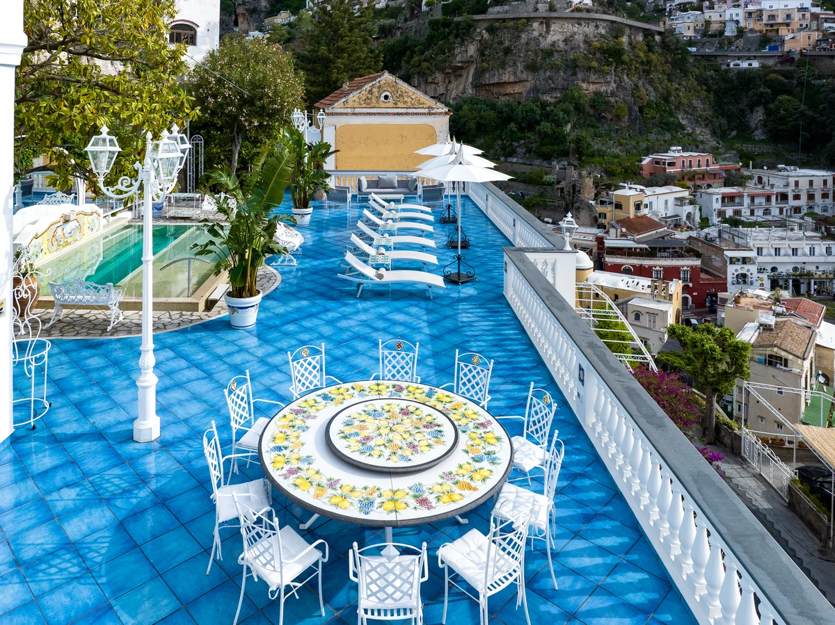 The blue-tiled roof terrace at Villa Mon Repos in Positano, with a round ceramic table, loungers and the pool above the village