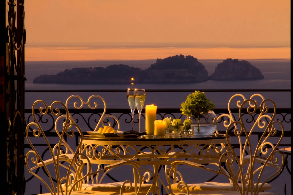 Candlelit terrace table laid for dinner above the sea, the islands beyond at sunset