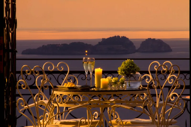 Candlelit terrace table laid for dinner above the sea, the islands beyond at sunset